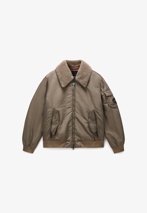 Chaqueta bomber marrón con cuello de piel, cierre de cremallera en el frente, bolsillos laterales y puños acanalados. Tela exterior suave con una apariencia ligeramente acolchada.