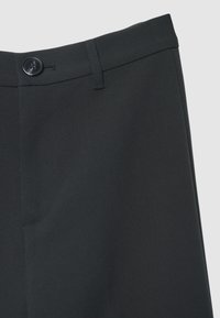 Pantaloni neri con una texture liscia e intrecciata, tasca frontale e chiusura con bottone in vita. Vestibilità sartoriale con linee pulite.