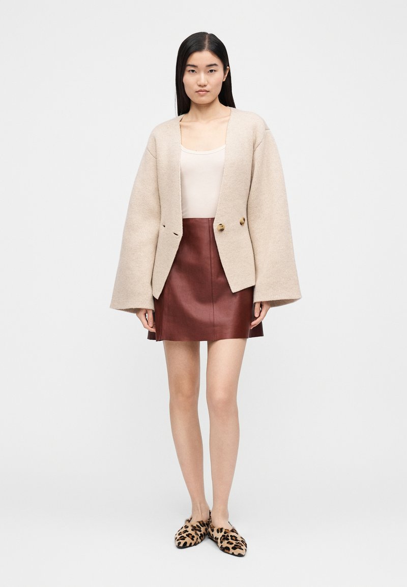 Beige oversized cardigan i uldblanding med vide ærmer, kombineret med en bordeaux lædernederdel i minilængde og loafers med leopardprint.