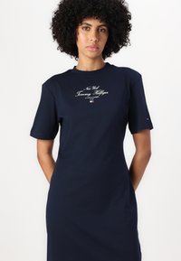 Tamno plava pamučna haljina s kratkim rukavima, s natpisom "New York Tommy Hilfiger" u bijelim i crvenim akcentima na prsima.