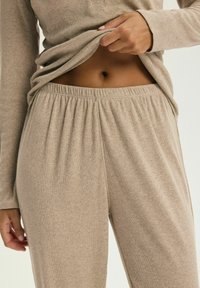 Jasnobrązowy zestaw odzieży codziennej z prążkowanego materiału, składający się z długiego rękawa bluzki i spodni z elastycznym paskiem w talii, wykonany z miękkiego, teksturowanego materiału.