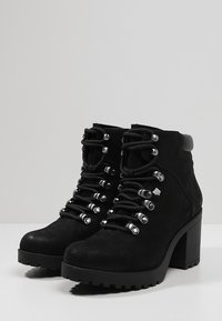 Zwarte enkellaarsjes van suède met een stevige hak, een ronde neus en zilverkleurige veterogen. Voorzien van veters en een geribbelde zool voor grip.