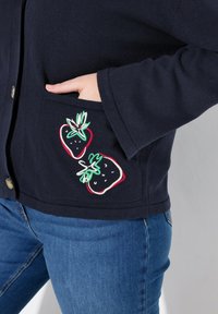 Mörkblå stickad cardigan med två broderade jordgubbar på fickan, med en avslappnad passform och knappstängning.