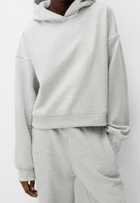 Sudadera con capucha de color gris claro, con un bolsillo frontal, hombros caídos y puños de canalé, hecha de una suave mezcla de algodón.