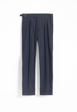 Pantalones ajustados azul marino con bolsillos laterales, pliegues, dobladillos con puños y un cinturón con hebilla sobre un fondo blanco liso.