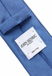 Sininen raidallinen kangastaita, jossa on ommeltu valkoinen etiketti, jossa lukee "JOHN HENRIC SWEDEN" ja "Made in Italy." Teksturoitu materiaali, jolla on sileä pinta.