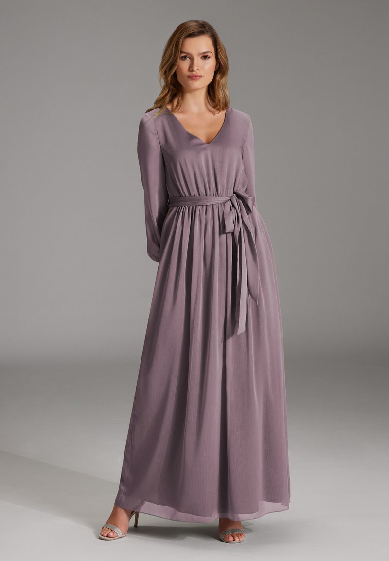 Langes Lavendelkleid mit V-Ausschnitt, langen Ärmeln und gebundenem Taillengürtel. Hergestellt aus einem fließenden Material, mit einem leicht transparenten Saum.