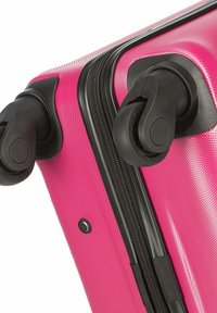 Valise rigide de couleur rose vif avec une surface texturée, roues noires et fermeture éclair. Dotée d'une finition lisse et de détails de design distincts.
