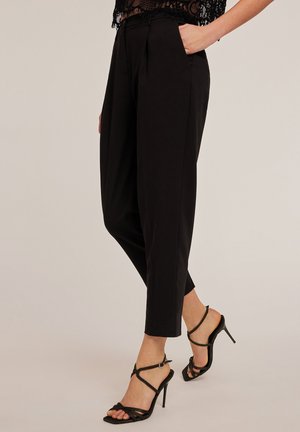 Pantalones negros ajustados con una cintura alta y pliegues, combinados con sandalias negras de tacón alto con tirantes. Textura suave y corte hasta el tobillo.