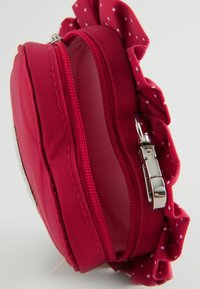 Rund rød nylon møntpunge med en struktureret overflade, sølv lynlås og en rynket prikket accent på toppen. Åbnet, der viser indvendigheden.