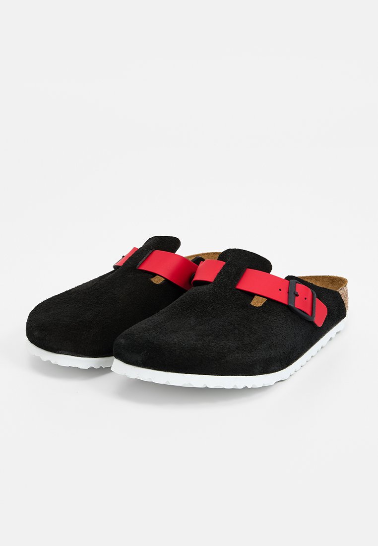 Sabots noirs à enfiler avec semelles blanches et sangles rouges réglables avec boucles noires, présentés sur un fond blanc.