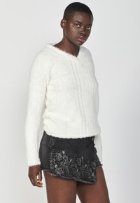 Valge, koheline pullover V-kaelusega ja pikkade gorete. Kombineeritud musta tikandiga mini-seelikuga, millel on frayed ääred.