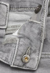 Țesătură de denim gri care arată un prim-plan al unei buzunare cu un nasture metalic argintiu și detalii de cusătură vizibile, având o textură ușor uzată.