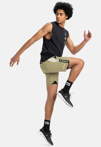 Top sin mangas negro con detalles gráficos; pantalones cortos caqui con bolsillos laterales y marca; calcetines negros y zapatillas deportivas con suela blanca.