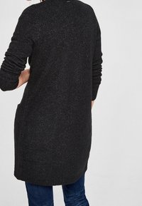 Cardigan lungo nero realizzato in tessuto a maglia testurizzata, con maniche lunghe, un colletto rotondo e tasche laterali.