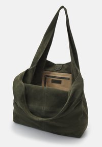 Sac à épaule en daim vert foncé avec une longue bandoulière, ouverture sur le dessus et poche intérieure zippée beige sur fond uni.