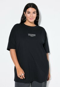 Sort oversized t-shirt lavet af bomuld med korte ærmer, med hvid broderet tekst på forsiden. Glat tekstur og afslappet pasform.