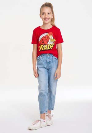 Rotes Baumwoll-T-Shirt mit „The Flash“-Grafik, kombiniert mit hellblauen Jeans und weißen Turnschuhen mit gemusterten Schnürsenkeln.