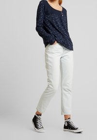 Marinblå långärmad skjorta med ett ljust mönster, treknäppt halsringning, parat med ljus denimjeans och svarta hög-top sneakers.