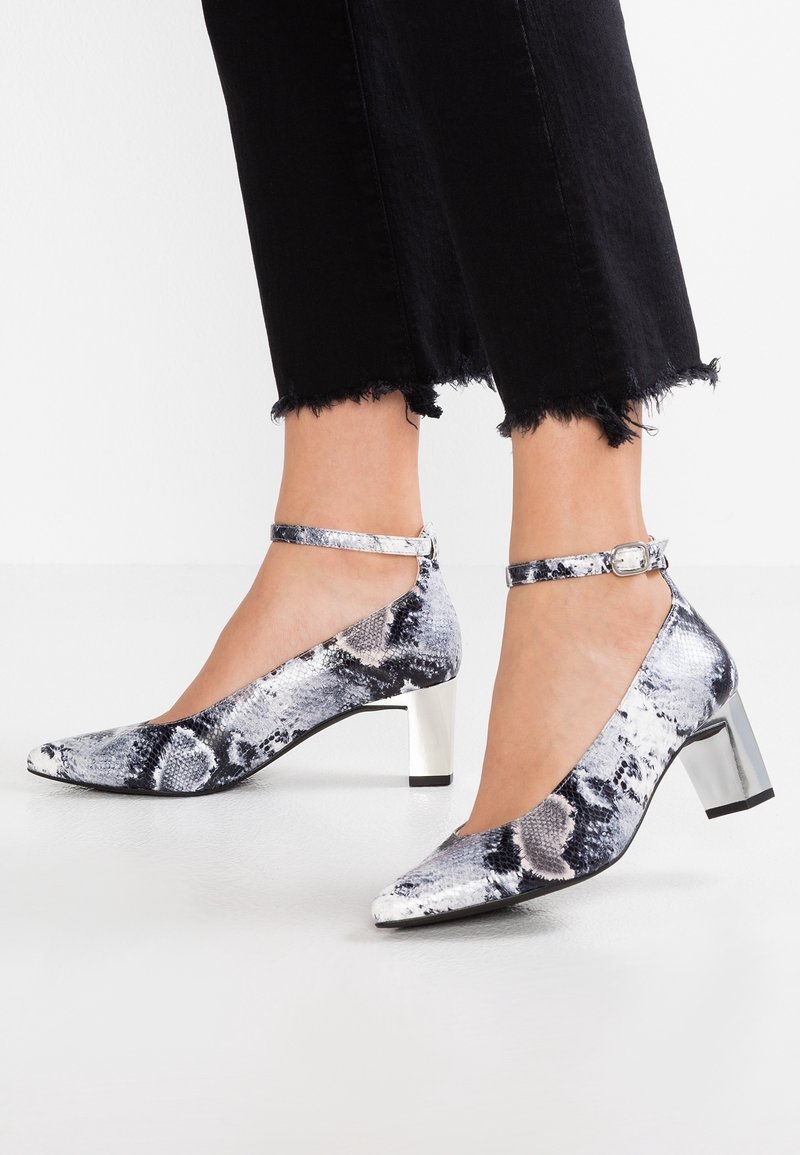 Escarpins à bout pointu avec un imprimé serpent noir et blanc. Comprend une bride de cheville et un talon bloc argenté. Texture lisse avec des accents brillants.