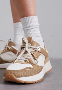 Beige og hvite sneakers med teksturert design, som har snøring, gummisåle og detaljer, kombinert med rillete hvite sokker.