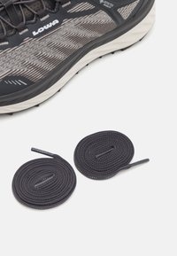 Chaussures de trail avec une tige texturée noire et grise, présentant un matériau Gore-Tex, et des lacets ronds noirs positionnés en dessous.