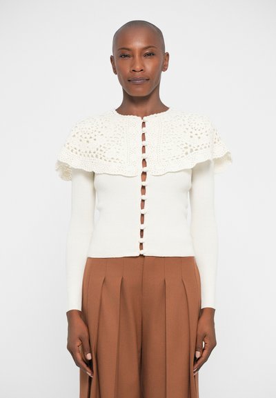 Cardigan lavorato a maglia color avorio con yoke in crochet testurizzato e chiusura con bottoni, dotato di maniche lunghe e silhouette aderente.