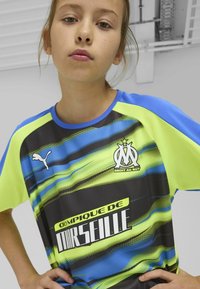 Puma noorte särk, millel on must alus, sinised ja neoonkollased graafilised triibud, võrkmaterjal ja Olympique de Marseille logo.
