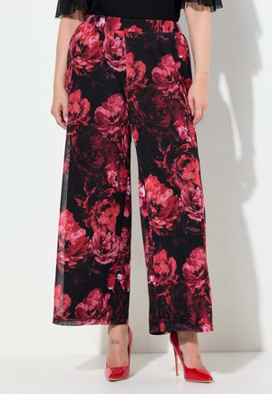 Pantaloni a palazzo floreali neri con grandi motivi di fiori rossi e rosa. Leggeri, con vita elastica, abbinati a tacchi alti rossi.