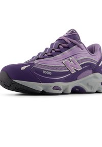 Μωβ αθλητικό παπούτσι με επάνω μέρος από δίχτυ και συνθετικό υλικό. Διαθέτει λαστιχένια σόλα, σχέδιο με κορδόνια και ανακλαστικές λεπτομέρειες. Μοντέλο 1000 από τη New Balance.