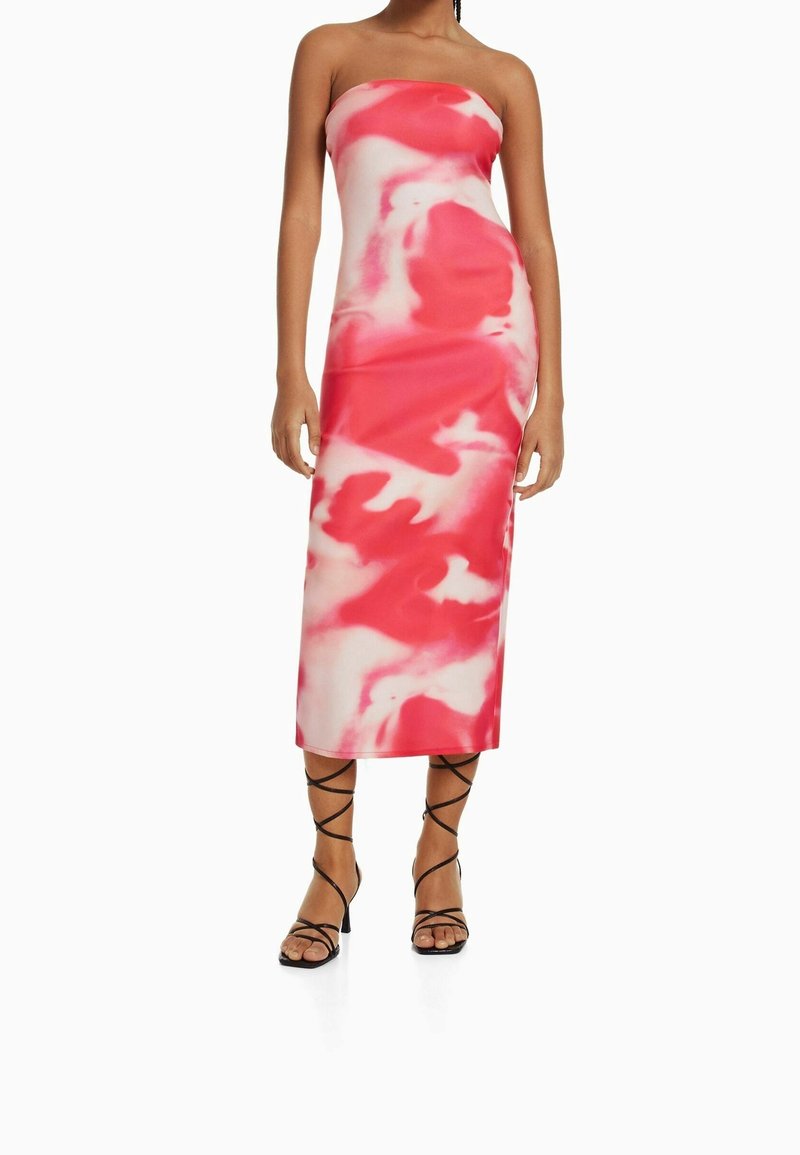 Robe midi sans bretelles marbrée rose et blanche au design ajusté, fabriquée en tissu lisse avec une silhouette élégante. Des sandales noires à lanières complètent le look.