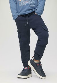Marine joggers met elastische boorden, zijzakken en een drawstring taille, gecombineerd met marine sneakers met witte zolen en rode accenten.