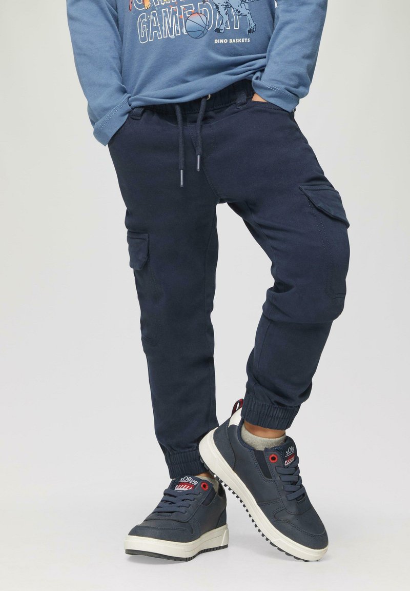 Marine joggers met elastische boorden, zijzakken en een drawstring taille, gecombineerd met marine sneakers met witte zolen en rode accenten.