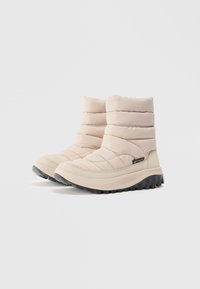 Stivali isolati beige chiaro con parte superiore trapuntata, suola in gomma e motivo a tacco circolare per una migliore aderenza. Presenta una piccola etichetta con logo nera.