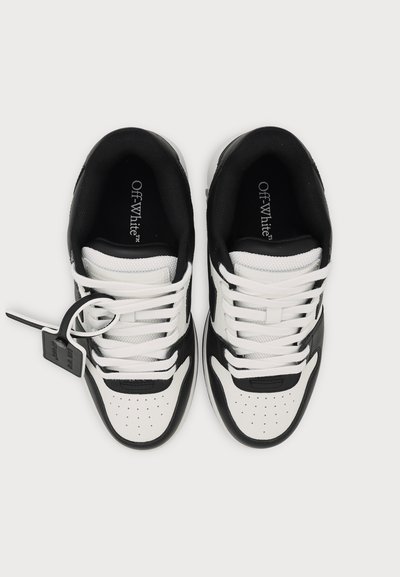Ζεύγος ασπρόμαυρα sneakers με την ένδειξη Off-White, με λευκά κορδόνια και μαύρη ετικέτα προσαρτημένη στο αριστερό παπούτσι σε λευκό φόντο.