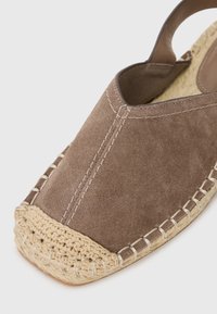 Espadrile din suede maro cu vârful rotunjit, având o talpă împletită din iută și cusături contrastante de-a lungul marginii.