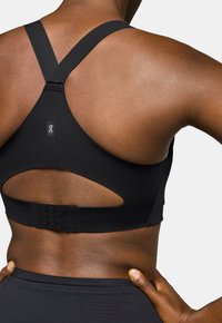 Sujetador deportivo negro con diseño de espalda cruzada, tela texturizada y corte en forma de llave. Cierre ajustable con gancho y ojal en la parte posterior.