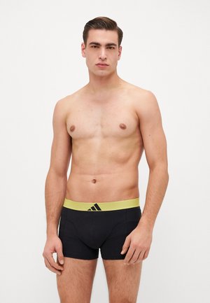 Schwarze Baumwoll-Boxershorts mit einem gelben Adidas-Logo am Bund, die einen eng anliegenden Sitz und kontrastierende Farbakzente aufweisen.