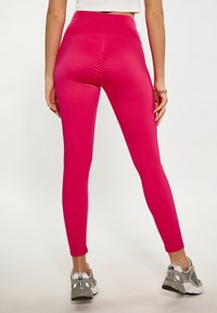Fuchsia legging met een hoge taille, een gladde textuur en een aansluitend ontwerp. De zijnaad loopt langs de benen. Gepaard met grijze sportschoenen.