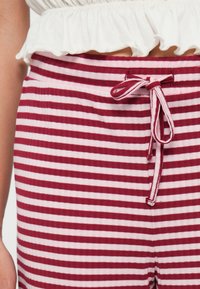 Calças listradas em vermelho e branco com uma textura suave, apresentando uma cintura elástica com cordão e um design leve e casual.