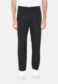 Pantaloni neri su misura con taglio dritto, davanti plissettato e una texture sottile. La vita presenta un bottone. Abbinati a sneakers bianche.