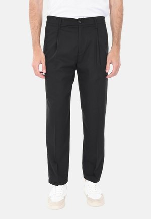 Pantaloni neri su misura con taglio dritto, davanti plissettato e una texture sottile. La vita presenta un bottone. Abbinati a sneakers bianche.