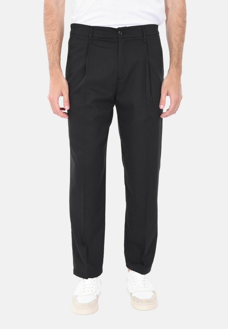 Pantaloni neri su misura con taglio dritto, davanti plissettato e una texture sottile. La vita presenta un bottone. Abbinati a sneakers bianche.