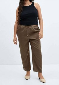 Haut noir sans manches et pantalon marron ample avec taille ajustable par cordon. Le mannequin porte des chaussures plates couleur nude. Design simple et couleurs neutres.