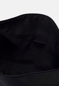 Černá látková taška uvnitř s kapsou na zip a hladkým povrchem. Nezdobený design s minimalistickou estetikou.