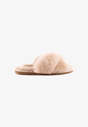 Chaussons beige clair flous avec des bandes croisées, fabriqués en matériau doux sur une semelle en caoutchouc marron plat. Texture pelucheuse sur toute la surface.