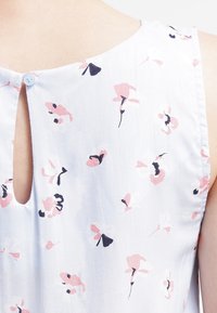 Helle blaue Bluse mit Blumenmuster aus weichem Stoff. Sie verfügt über eine Schlüsselöffnungs-Rückenpartie mit einem Knopf und ein Muster aus rosa und marineblauen Blumen.