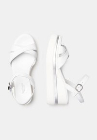 Sandales à plateforme blanches en cuir avec des brides croisées et une boucle ajustable à la cheville, présentant une semelle texturée blanche et des accents argentés.
