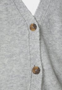Tissu tricoté gris clair avec deux boutons ronds marron fixés verticalement sur un vêtement à col en V.