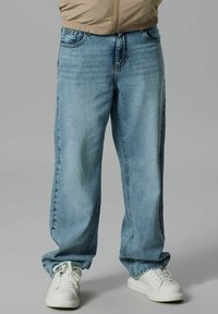 Jeans en denim bleu clair avec une coupe décontractée, dotés d'une fermeture à bouton et à fermeture éclair, de poches latérales et d'un décoloré subtil. Associés à des baskets blanches.